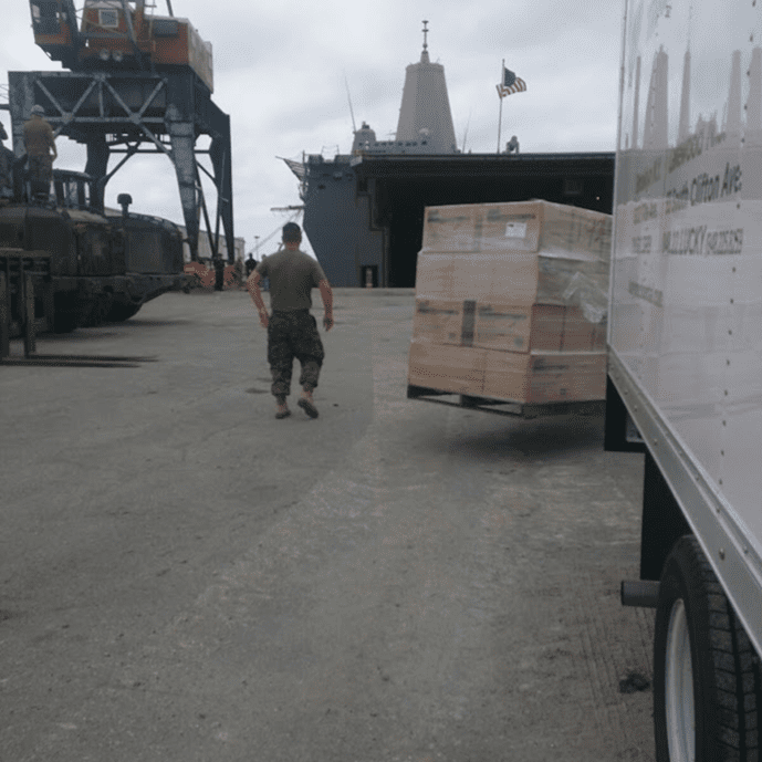 Forklift operator skillfully stacks pallets on a dock near a ship.