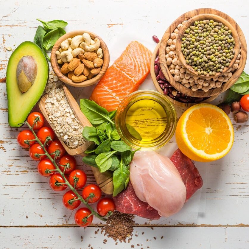 A colorful spread of healthy foods including avocado, salmon, nuts, and fresh vegetables.
